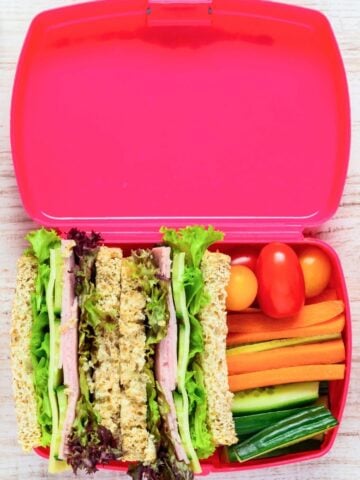 ham and cucumber sandwich with veggies in a pink lunchbox
