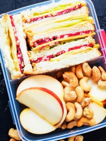 small lunch container with salami sandwich, apple slices and nuts
