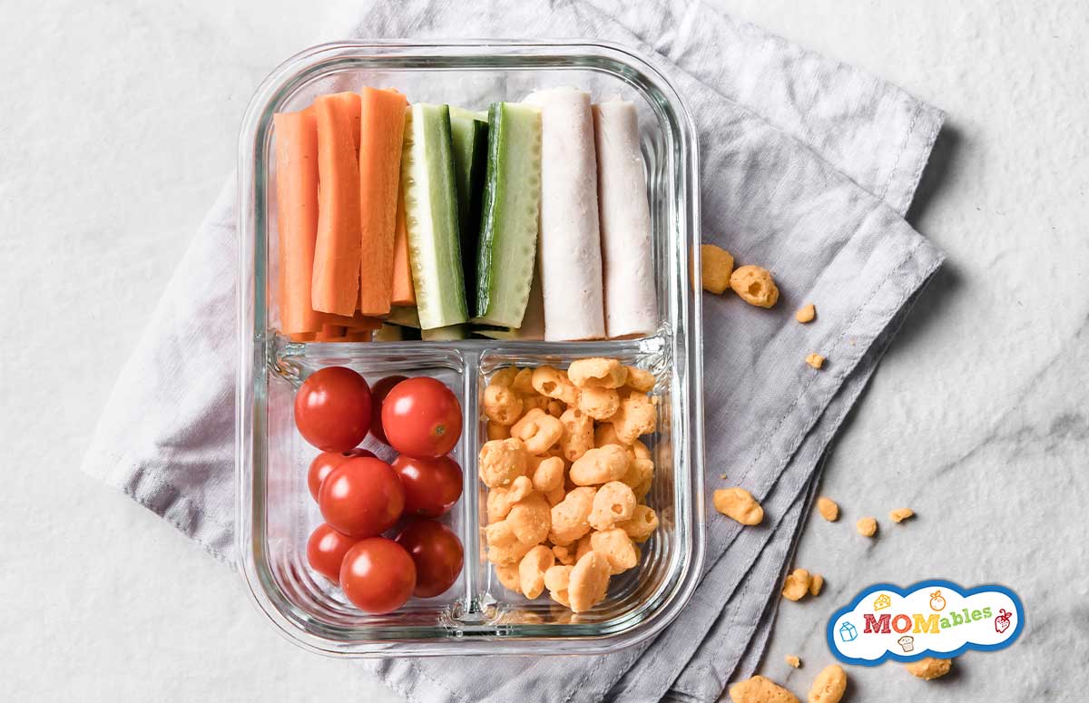a small snack container with turkey, veggies and snacks on a countertop with a gray kitchen towel