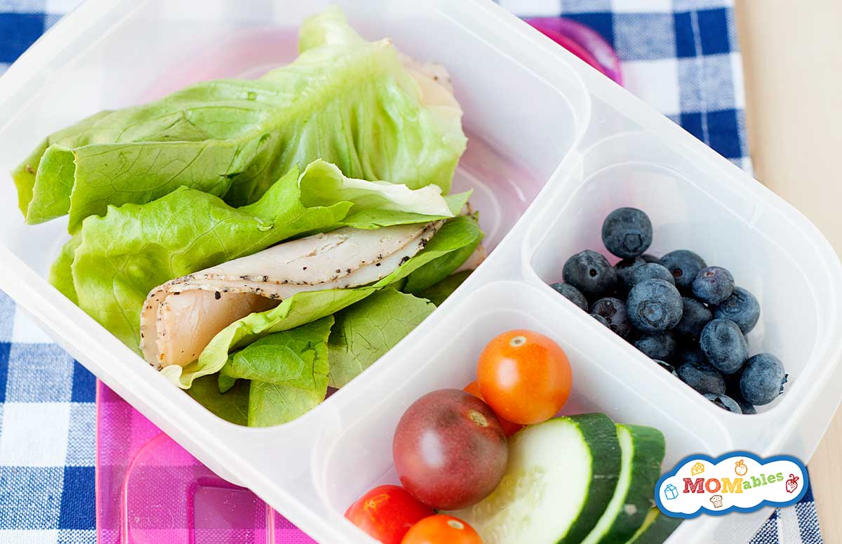 lettuce wraps with pepper turkey lunch meat in a lunch container with blueberries and veggies