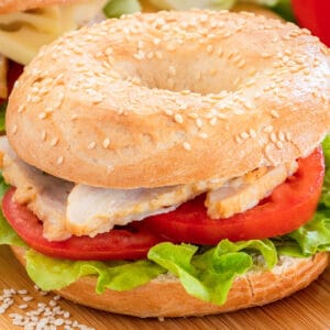 closeup of a bagel sandwich with chicken, tomato slices and lettuce