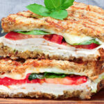 two halves of a grilled turkey sandwich with mozzarella, tomatoes and spinach.