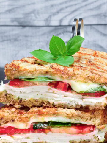 two halves of a grilled turkey sandwich with mozzarella, tomatoes and spinach.