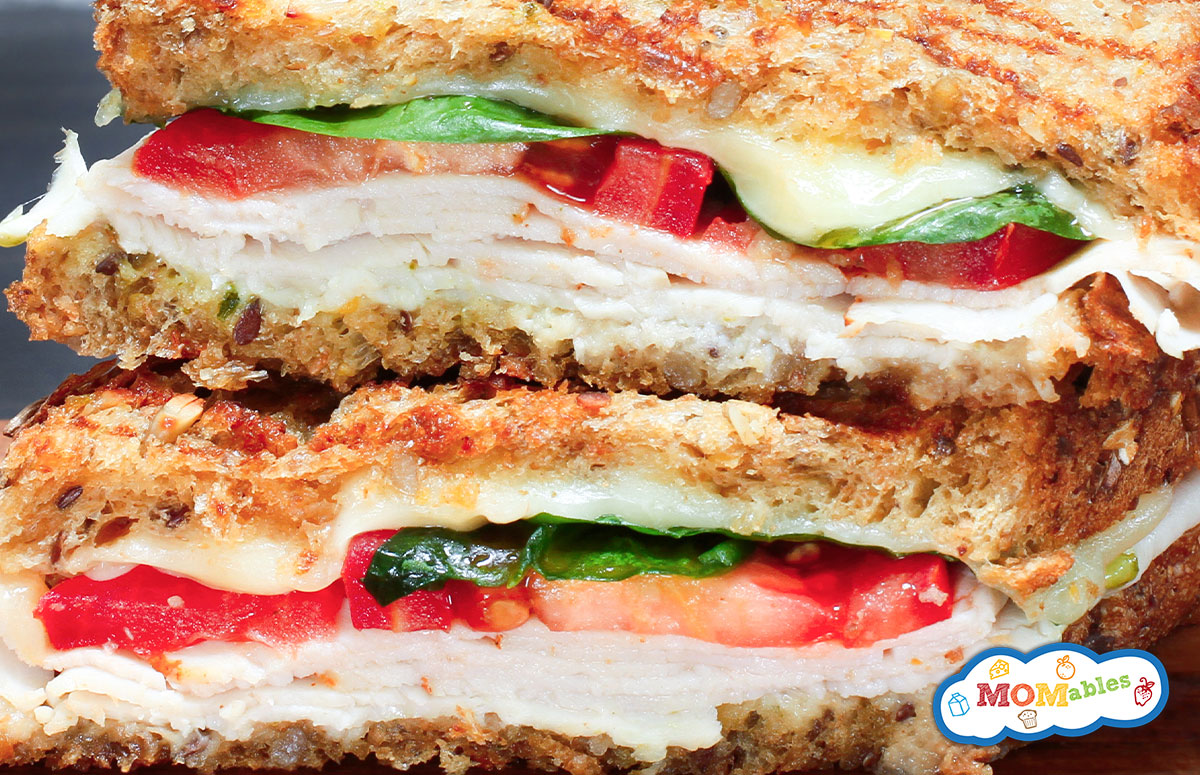 two halves of a grilled turkey sandwich with mozzarella, tomatoes and spinach.