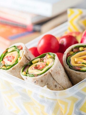ham and veggie wraps in a lunch container with cherry tomatoes