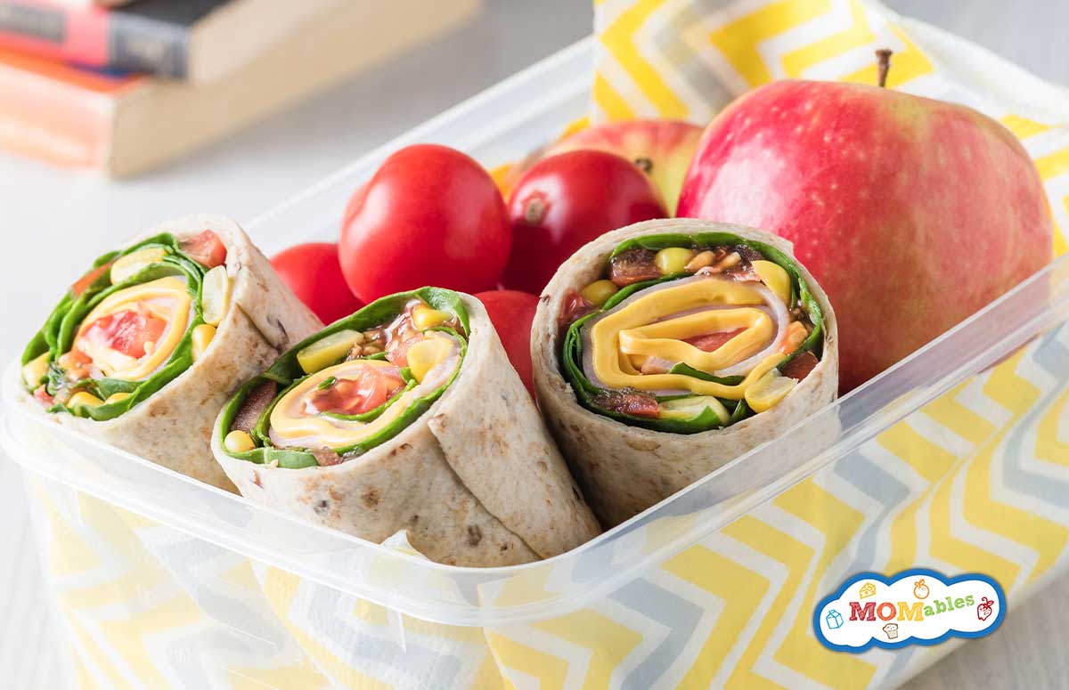ham and veggie wraps in a lunch container with cherry tomatoes and an apple