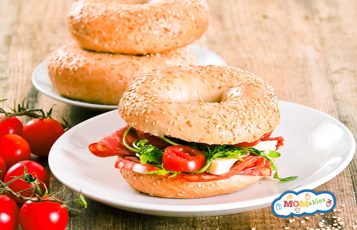 a salami bagel sandwich on a plate with two bagels behind it