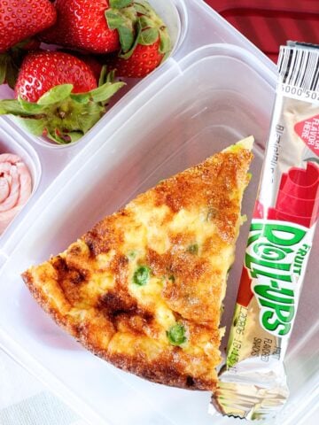 slice of quiche, fruit roll ups and fruit in a lunch container.