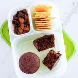 three chocolate muffins in a bento box with crackers and mixed nuts
