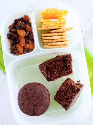 three chocolate muffins in a bento box with crackers, nuts and raisins