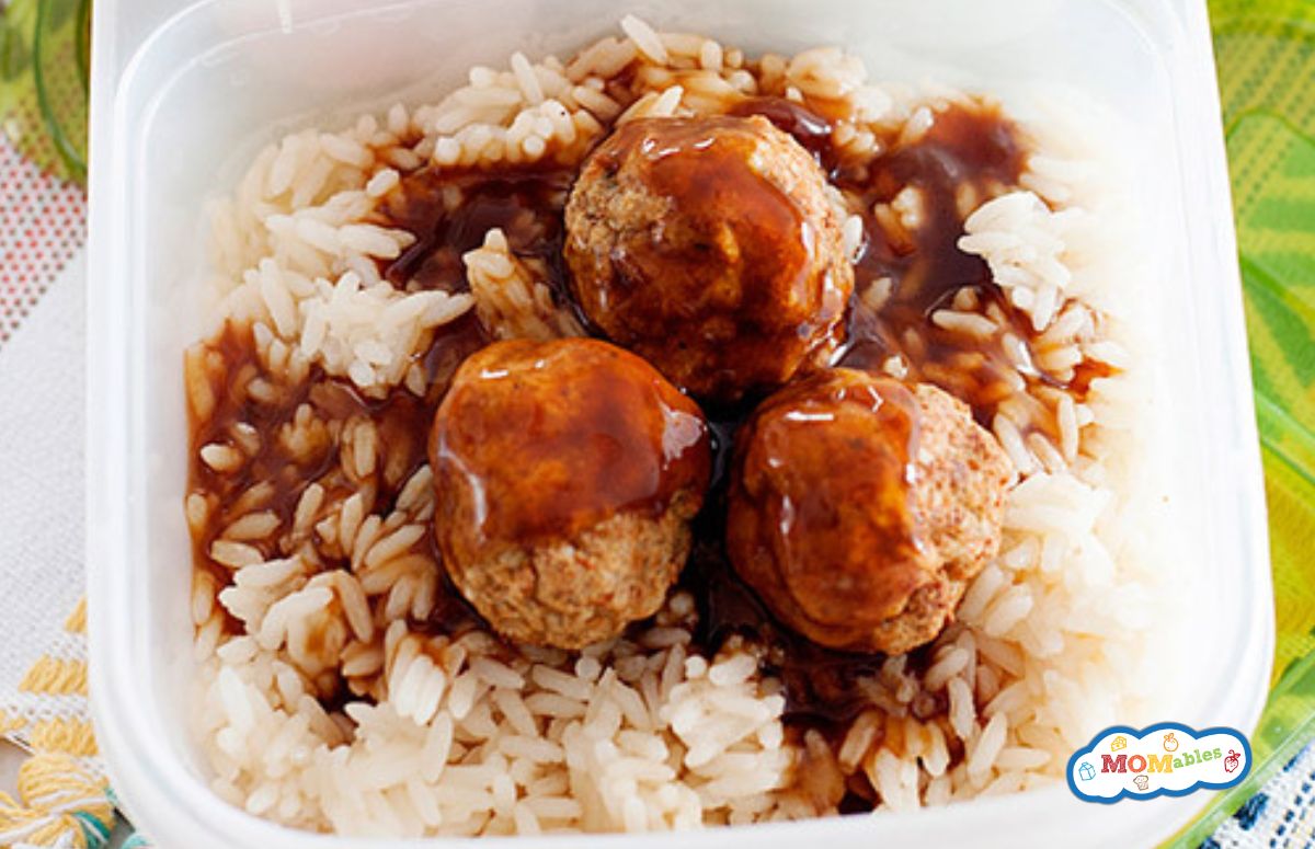 four meatballs over rice with gravy in a lunch container