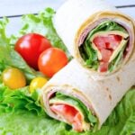 two halves of an Italian sandwich wrap with cherry tomatoes on the side