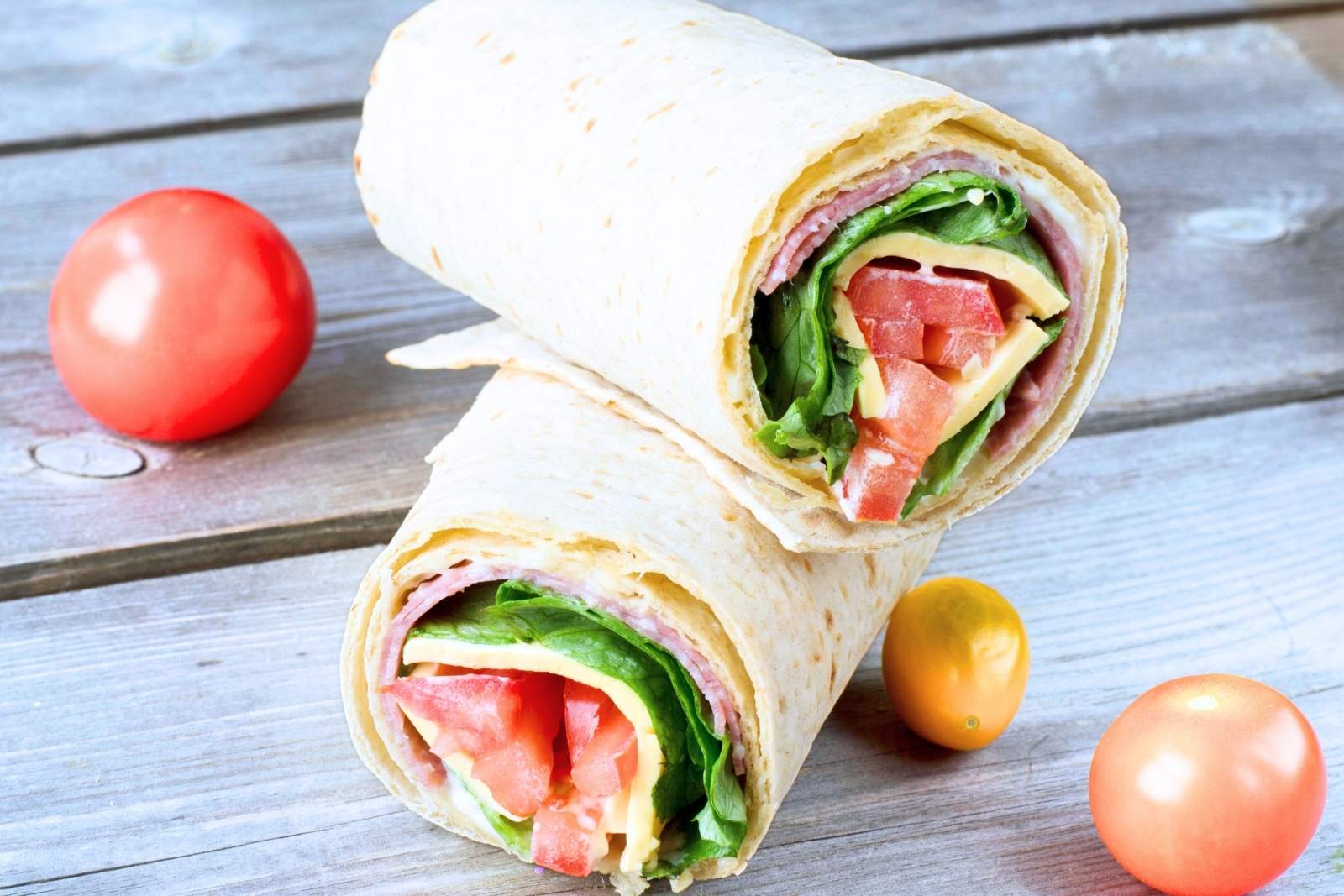 two halves of an Italian sandwich wrap on a countertop with cherry tomatoes