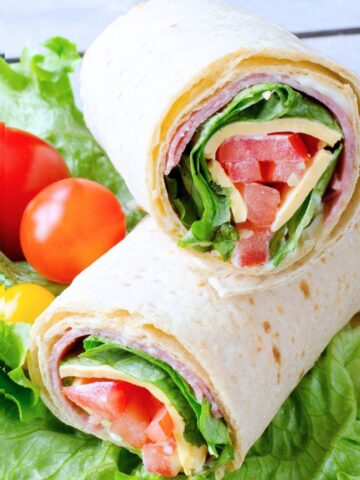 two halves of an Italian sandwich wrap with cherry tomatoes on the side