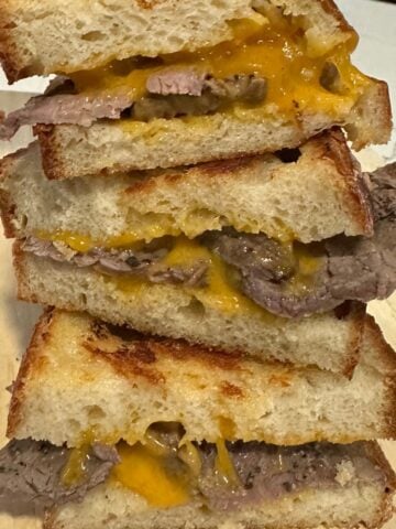 roast beef grilled cheese sandwiches stacked on a cutting board