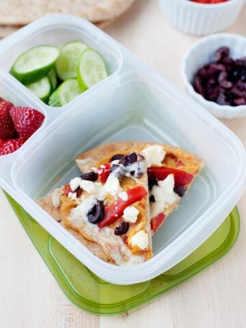 a lunch container with two slices of pita pizza, cucumber slices and strawberries in it