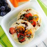 caprese english muffins in a bento box with blueberries and carrot sticks