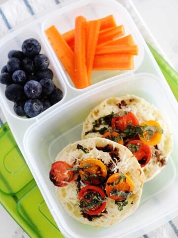 caprese english muffins in a bento box with blueberries and carrot sticks