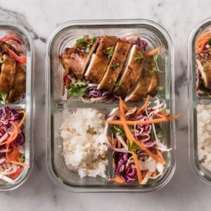 a lunchbox with korean chicken, rice, and veggies