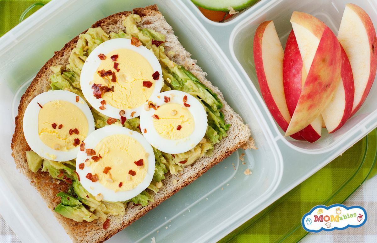 top view of a lunchbox with avocado toasts and a sliced apple