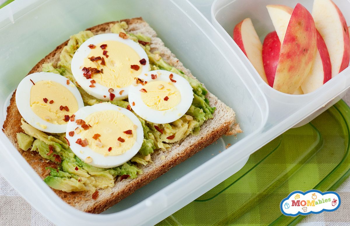 top view of a lunchbox with avocado toasts and a sliced apple