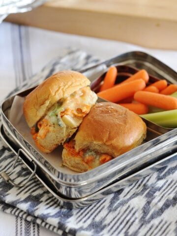 lunchbox with 2 buffalo chicken sliders and some veggies on the side