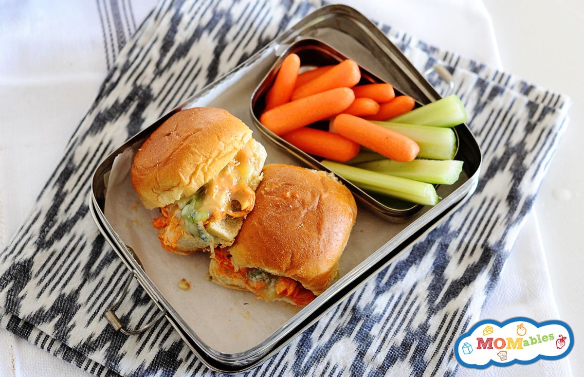 top view of a lunchbox with 2 buffalo chicken sliders and some veggies on the side