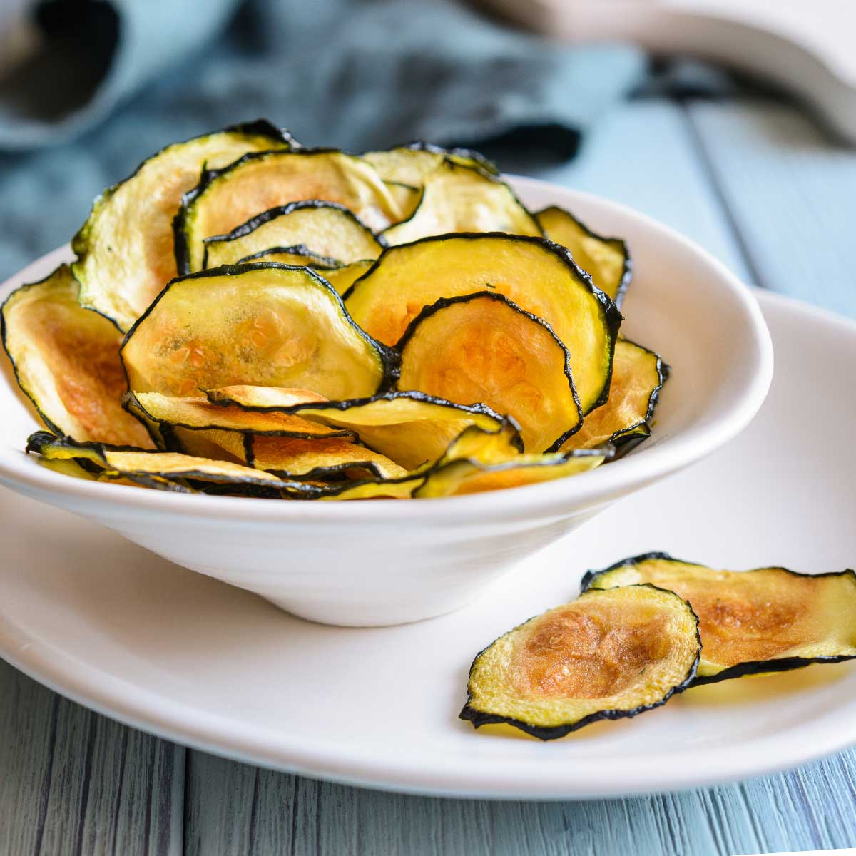 small white bowl with zucchini chips with 2 chips on the outside of bowl