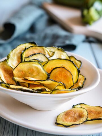 small white bowl with zucchini chips with 2 chips on the outside of bowl